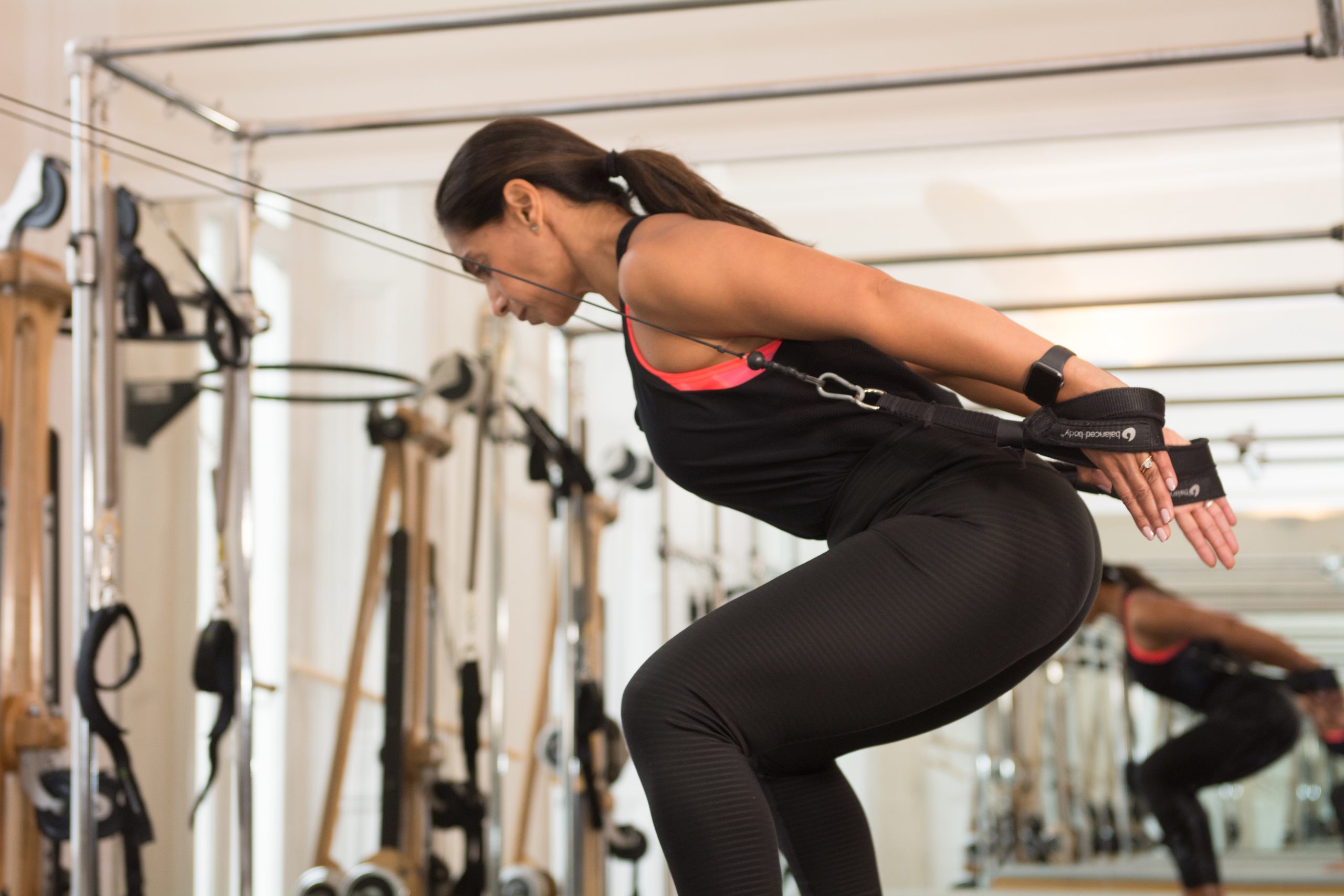 Client performing a standing hip hinge using arm springs on the Cadillac during a one-to-one classical Pilates session at Trevor Blount Pilates