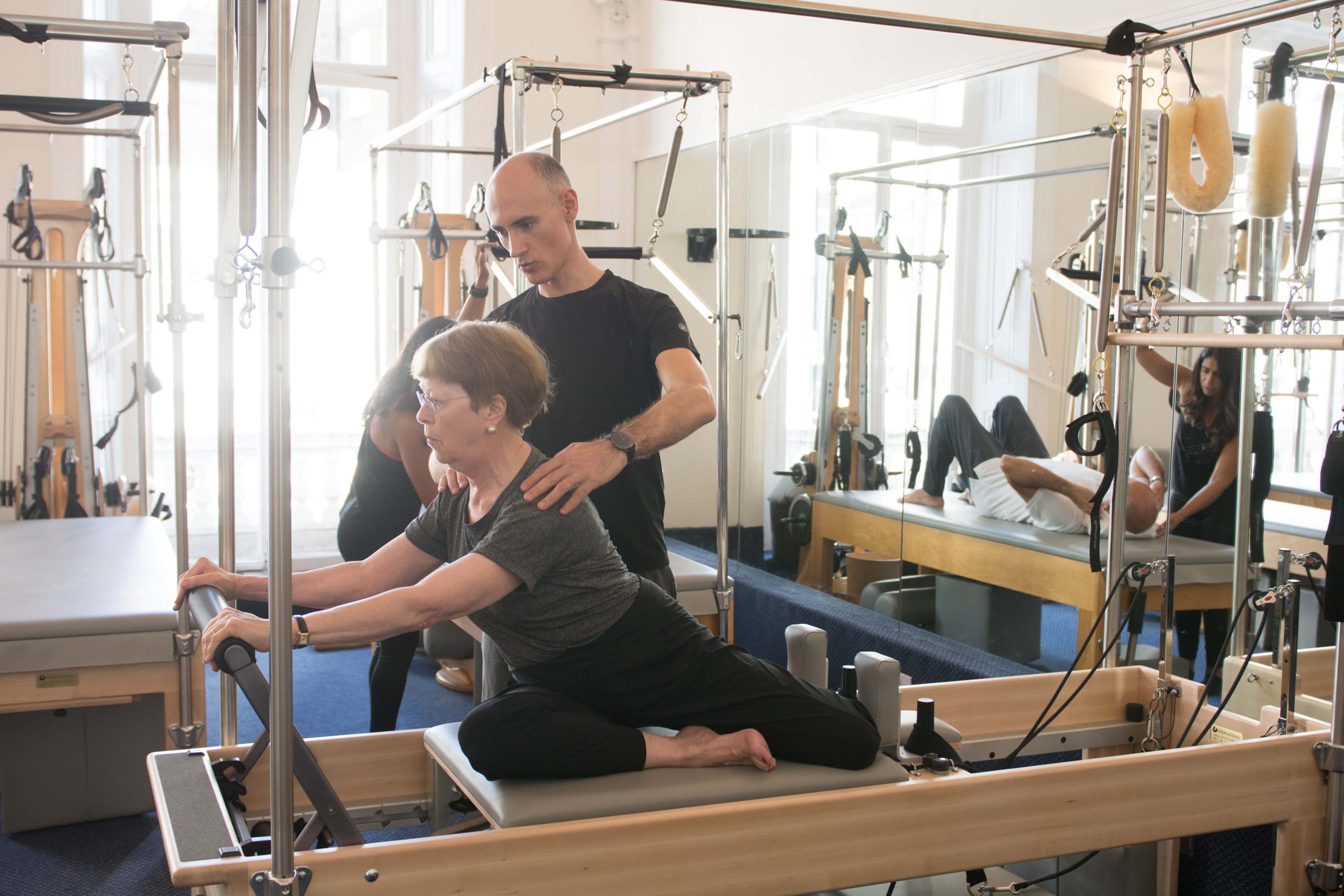 Instructor guiding an older client through a seated reformer stretch at a South Kensington Pilates studio